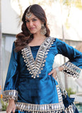 Woman wearing a blue traditional outfit with silver embellishments outdoors.