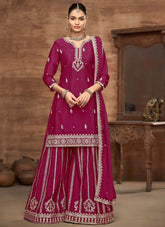 Woman wearing a traditional pink outfit with intricate white embroidery in a warm-toned room.