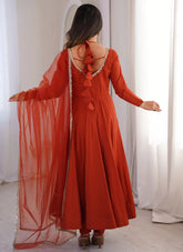 Woman wearing a red dress with a sheer overlay in a softly lit room.