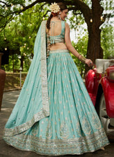 Woman in a light blue traditional outfit with a floral headpiece, standing outdoors.