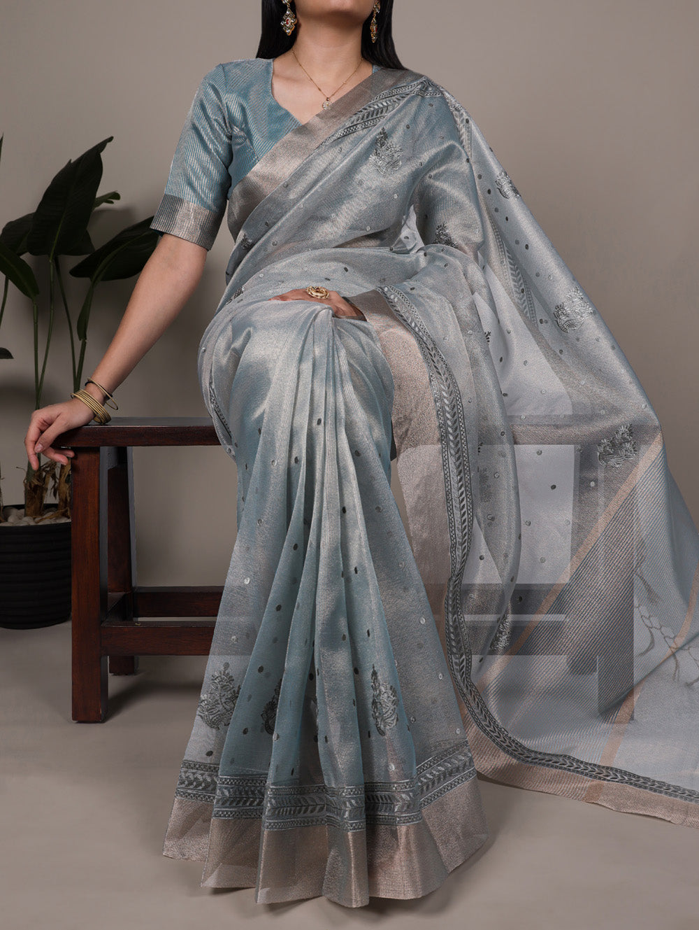 Woman wearing a light blue saree with a subtle pattern, sitting on a chair.