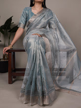 Woman wearing a light blue saree with a subtle pattern, sitting on a chair.