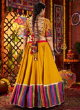 Woman in a vibrant yellow traditional outfit with colorful patterns in a decorated setting.