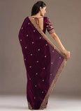 Woman wearing a purple saree with gold embroidery against a neutral background
