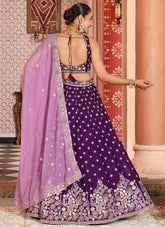 Woman in a purple and pink traditional outfit with intricate designs in a decorated room.