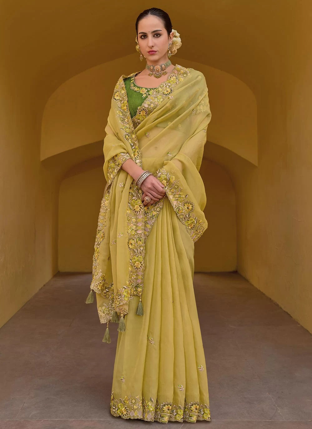 Woman wearing a yellow saree with floral patterns in an archway.