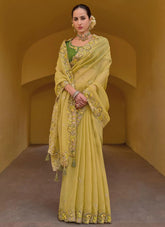Woman wearing a yellow saree with floral patterns in an archway.