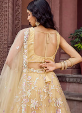 Woman in a yellow embroidered outfit with a floral pattern, standing against a textured wall.