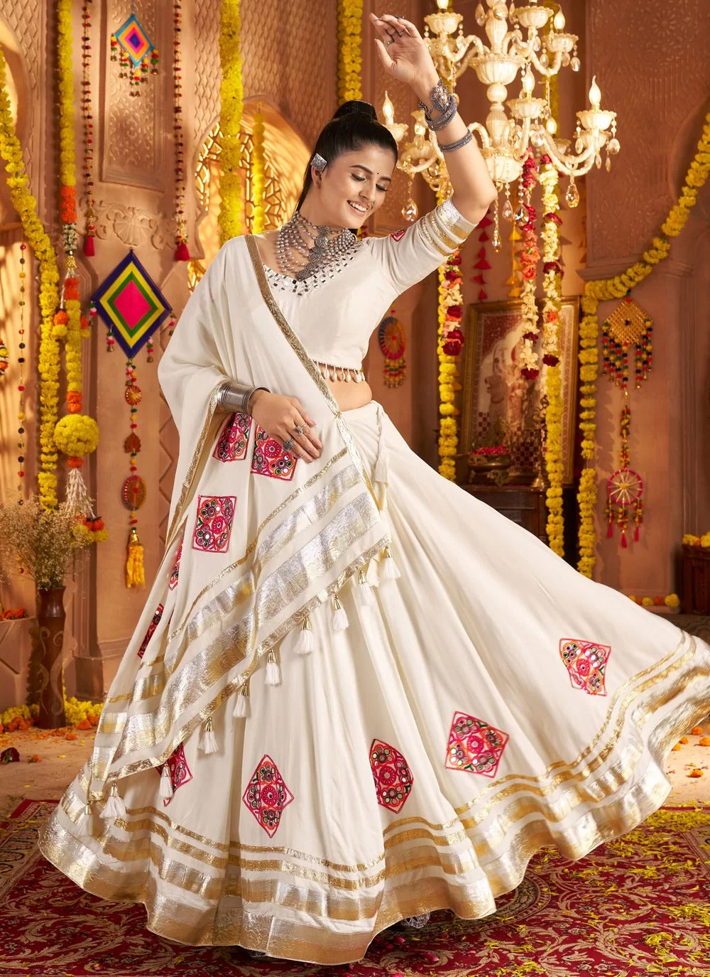 Woman in a traditional white saree with red and gold patterns, dancing in a decorated indoor setting.