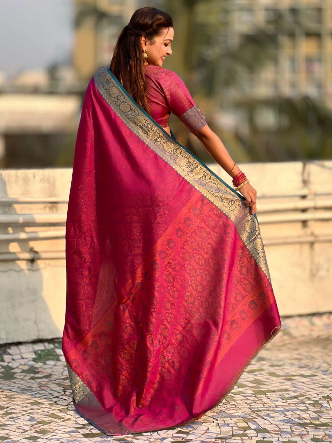Woman holding a red saree with a patterned border outdoors.