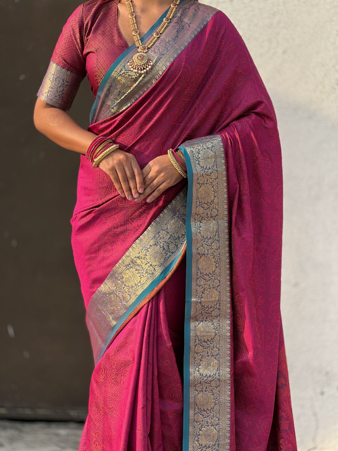Woman wearing a traditional maroon saree with a blue border against a neutral background