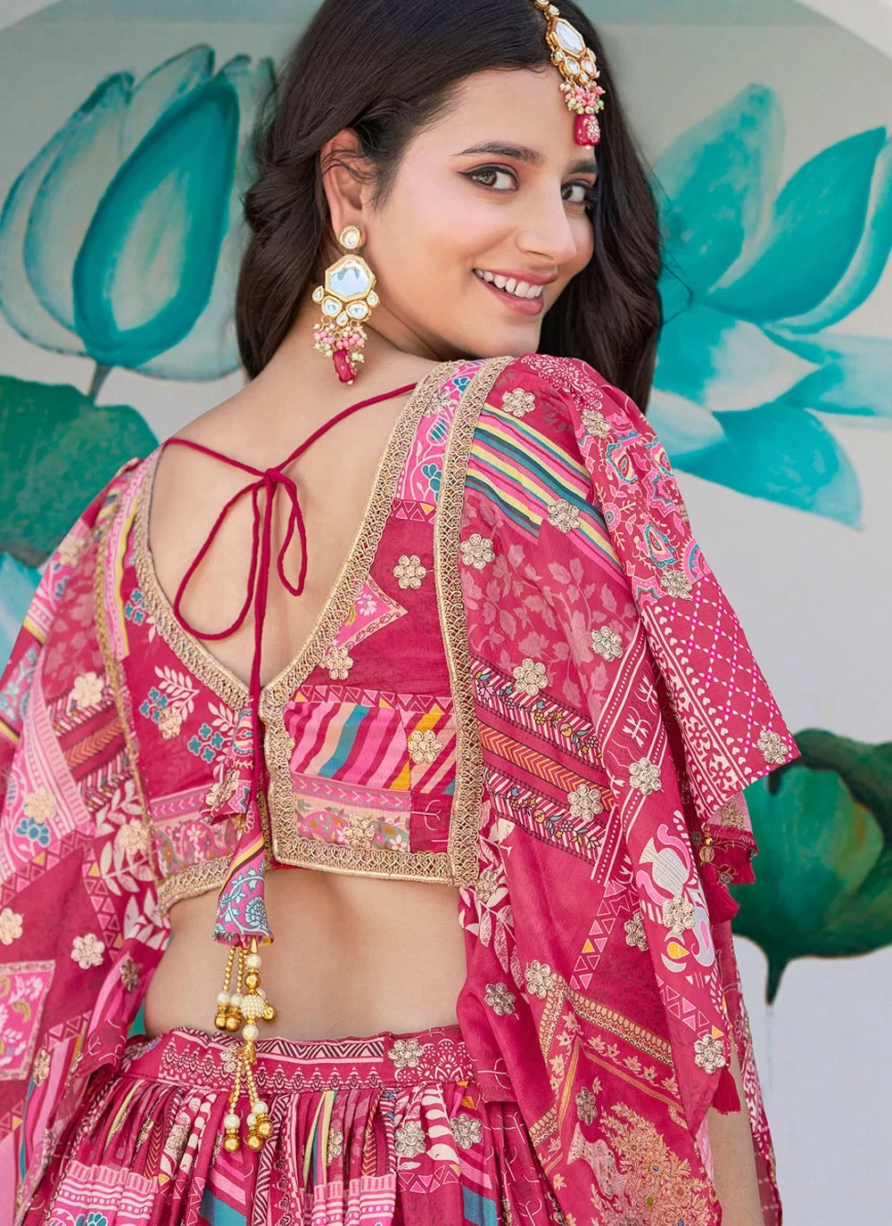 Woman wearing a traditional pink and gold embroidered outfit with a colorful dupatta against a decorative background.