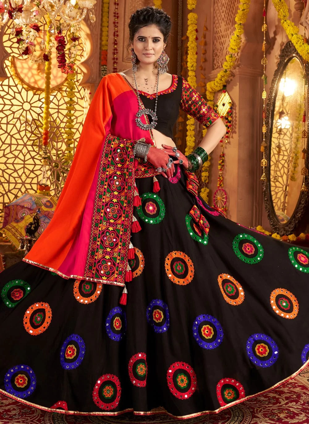 Woman in traditional black and red embroidered outfit with colorful patterns, standing against a decorative background.