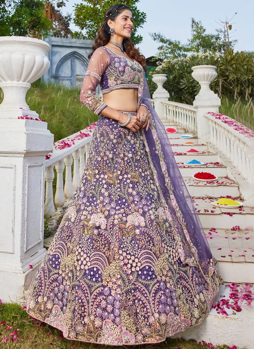 Woman in a purple and gold embroidered traditional outfit standing on a decorative staircase with flowers.