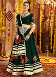 Woman in a traditional green and white outfit with jewelry in a decorated indoor setting.