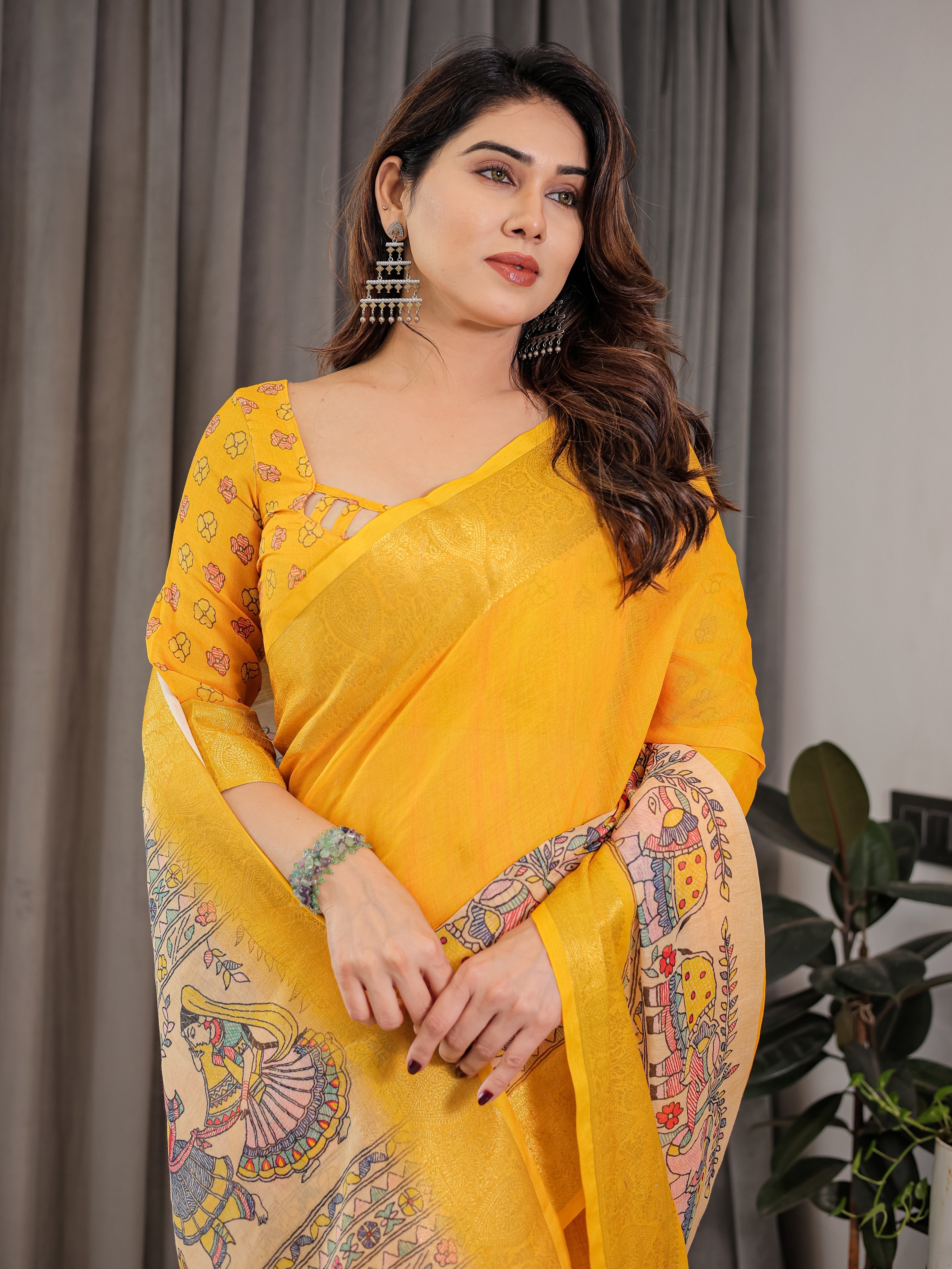 Woman wearing a yellow saree with intricate patterns, standing against a neutral background.