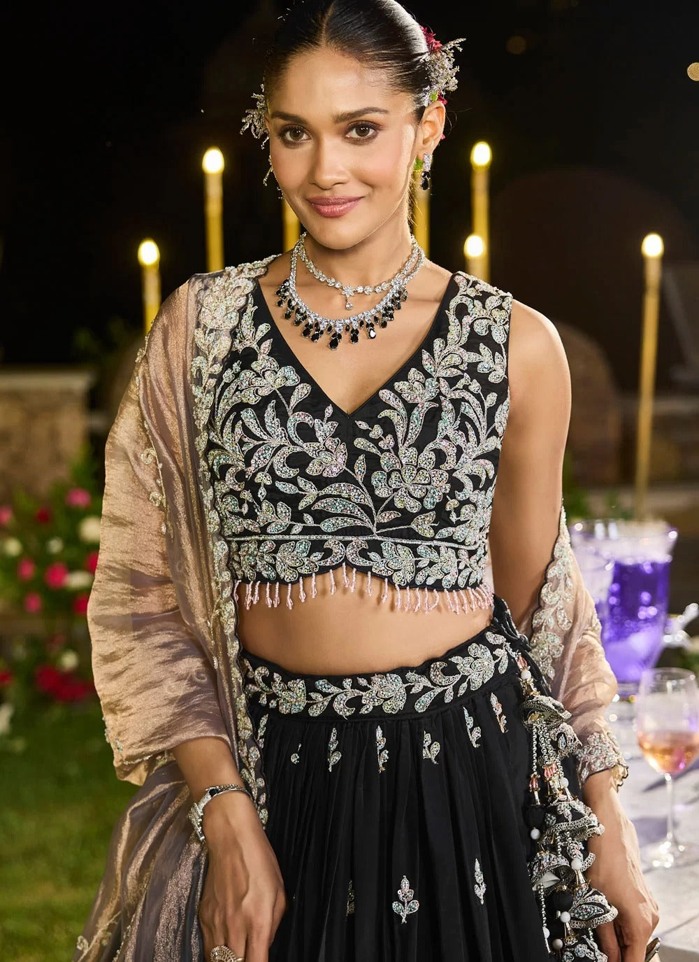 Woman in traditional black and silver embroidered outfit with jewelry, standing outdoors at night.