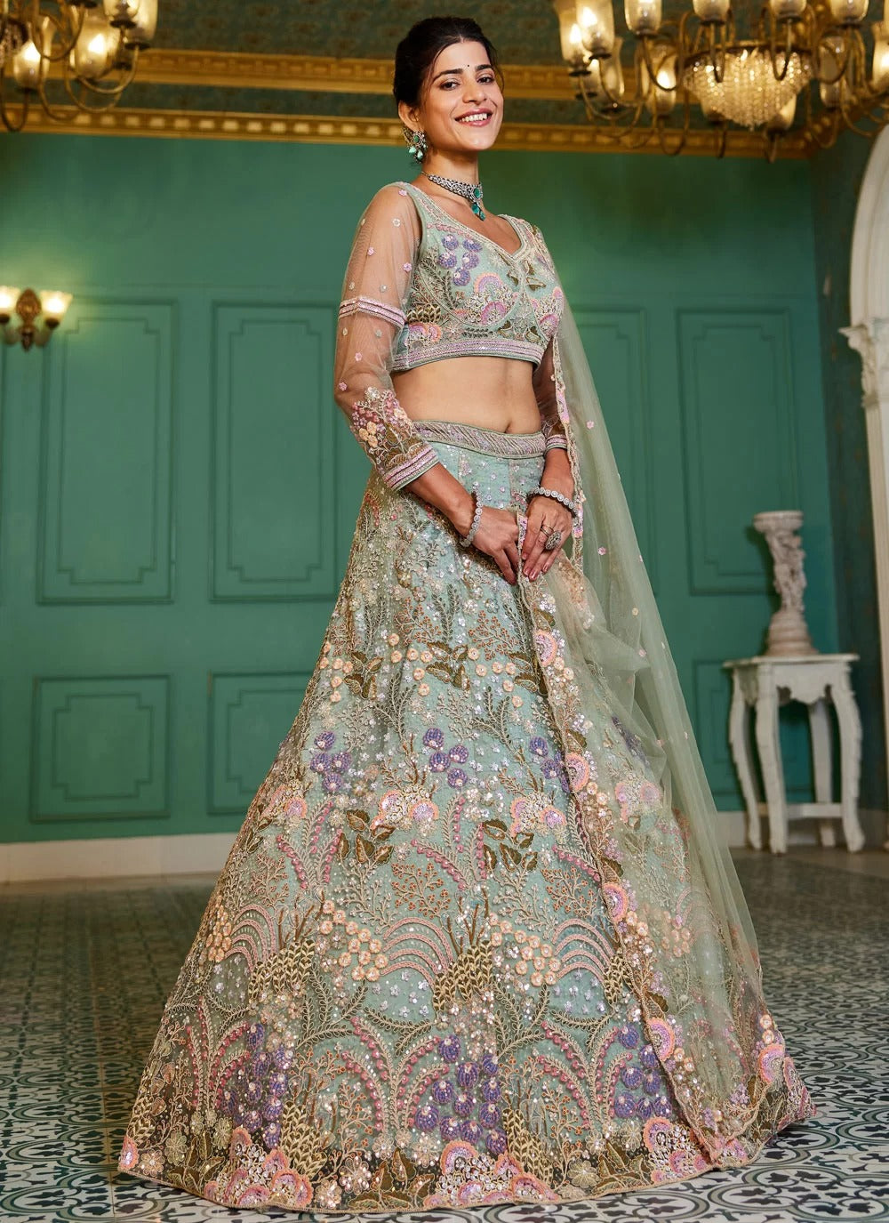 Woman in a traditional embroidered outfit standing in an elegant room with green walls and chandeliers.