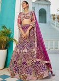 Woman in a traditional embroidered outfit with a pink dupatta standing in front of a blue wall.
