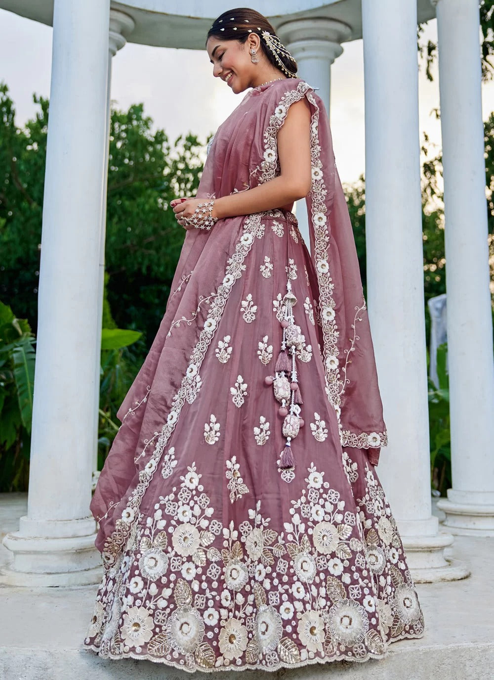 Woman in a mauve embroidered traditional outfit standing in front of white columns.