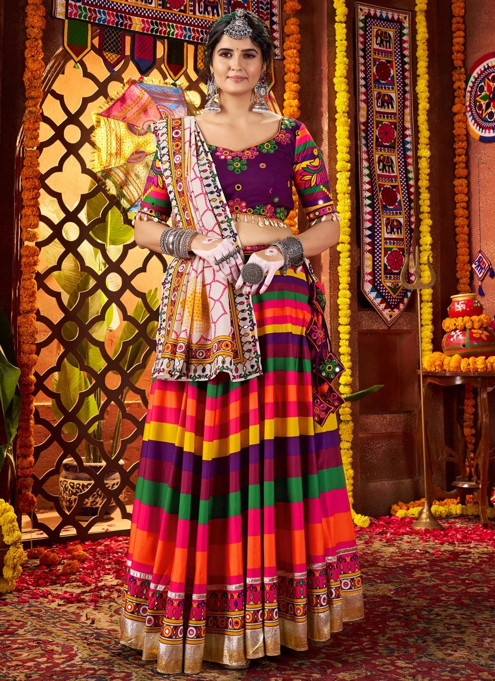 Woman in a colorful traditional outfit standing in a decorated indoor setting.