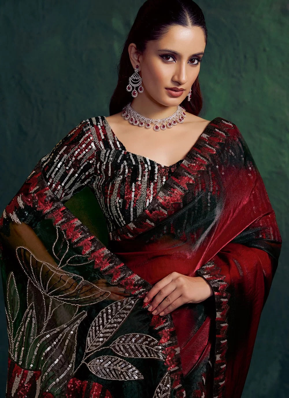 Woman wearing a traditional saree with intricate designs and jewelry against a dark background