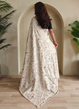 Woman wearing a floral saree standing in a room with plants.