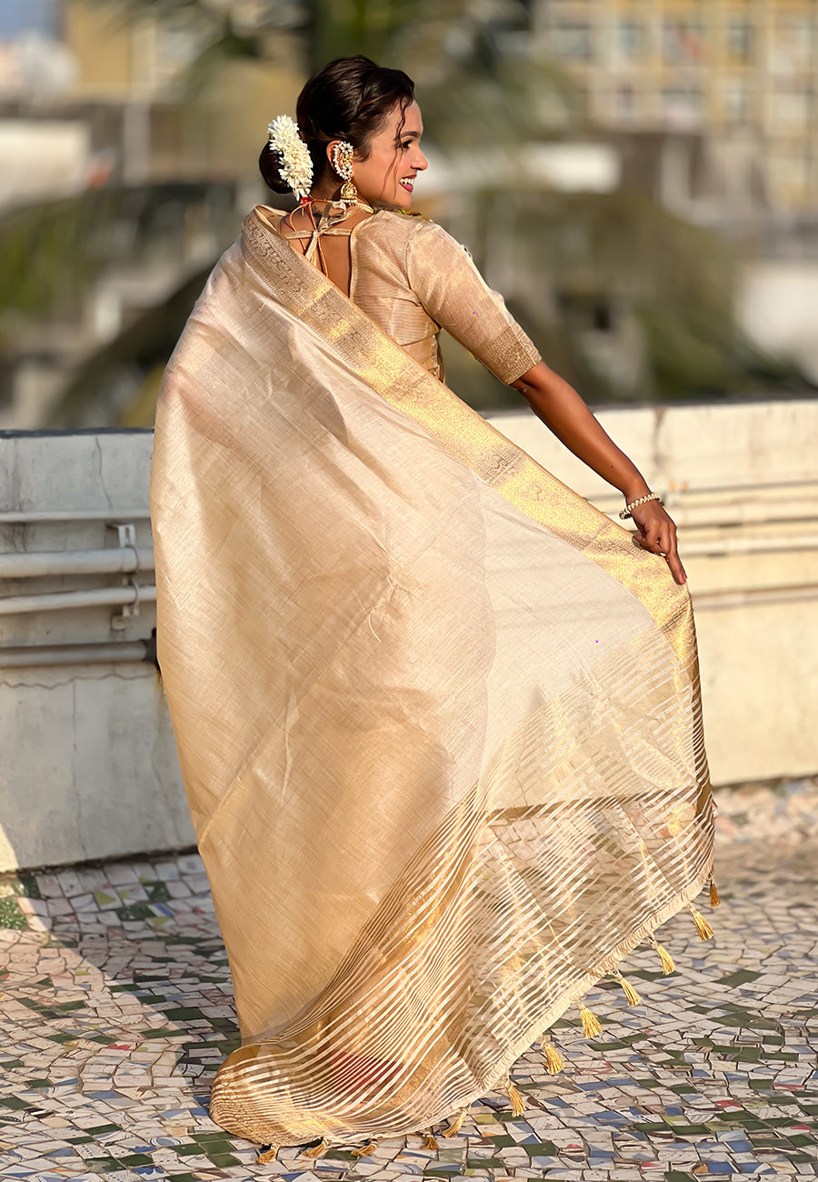 Woman in a beige saree standing outdoors with blurred background