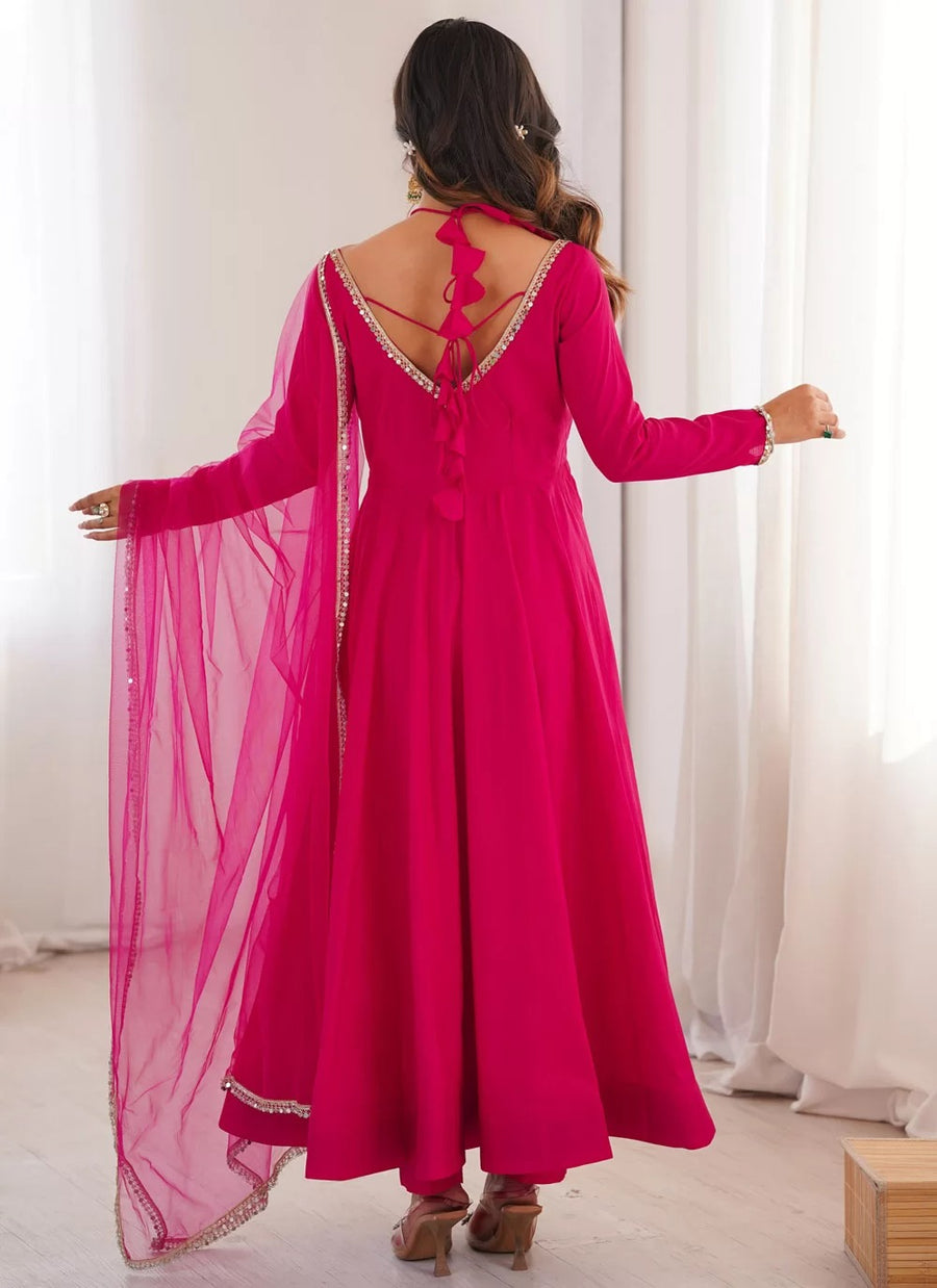 Woman wearing a bright pink traditional outfit with a sheer dupatta in a well-lit room.