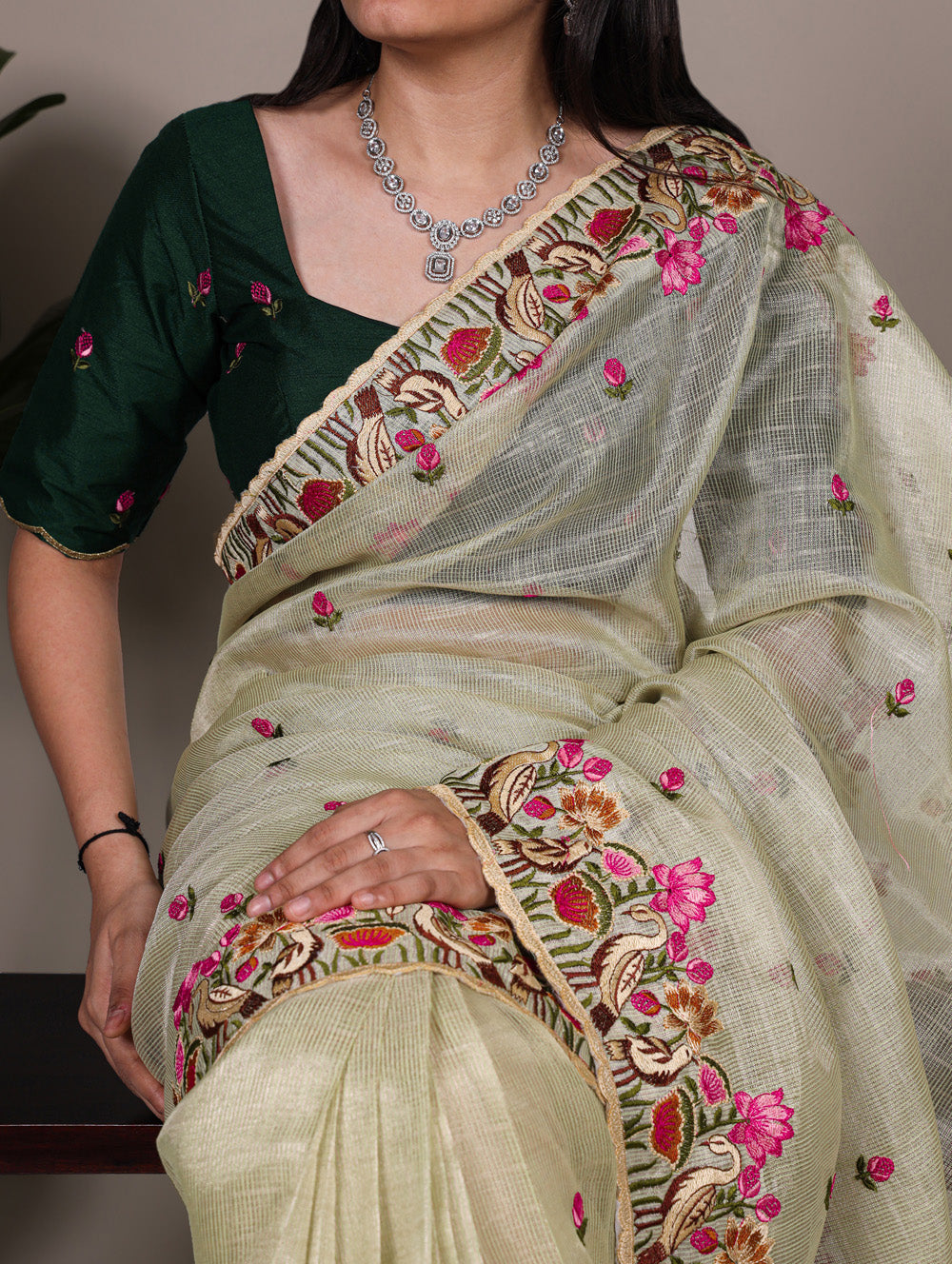 Woman wearing a light green saree with floral embroidery and a dark blouse.