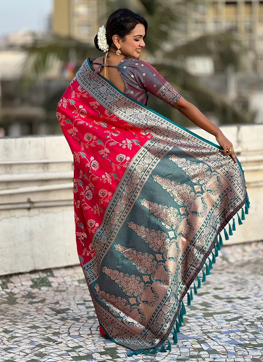 Woman holding a traditional saree with a red and blue pattern on a stone pavement.