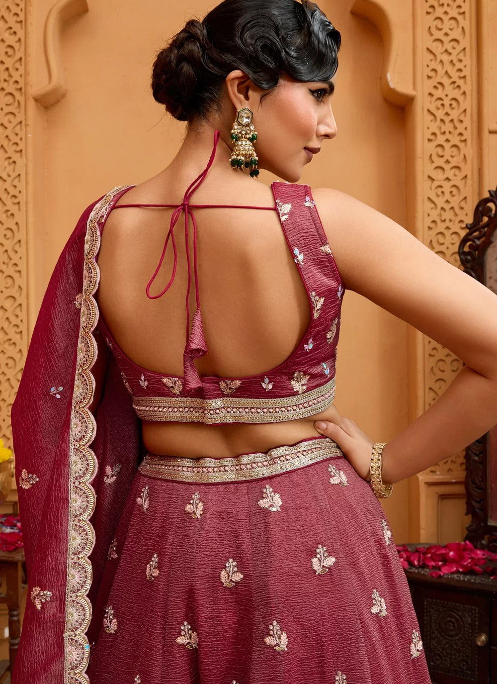 Woman in a traditional maroon embroidered outfit with a beige background
