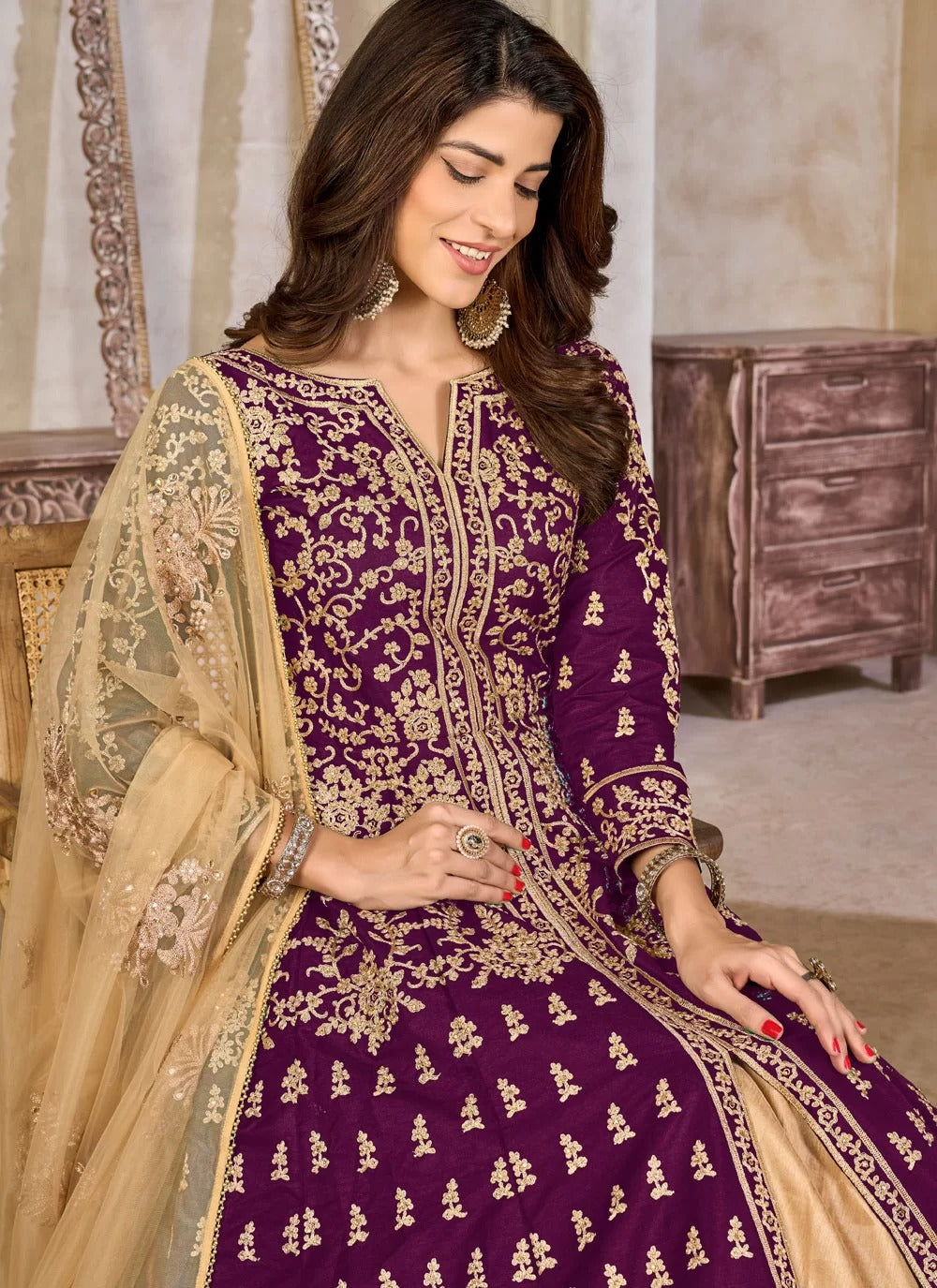Woman wearing a purple embroidered traditional outfit with gold details indoors.