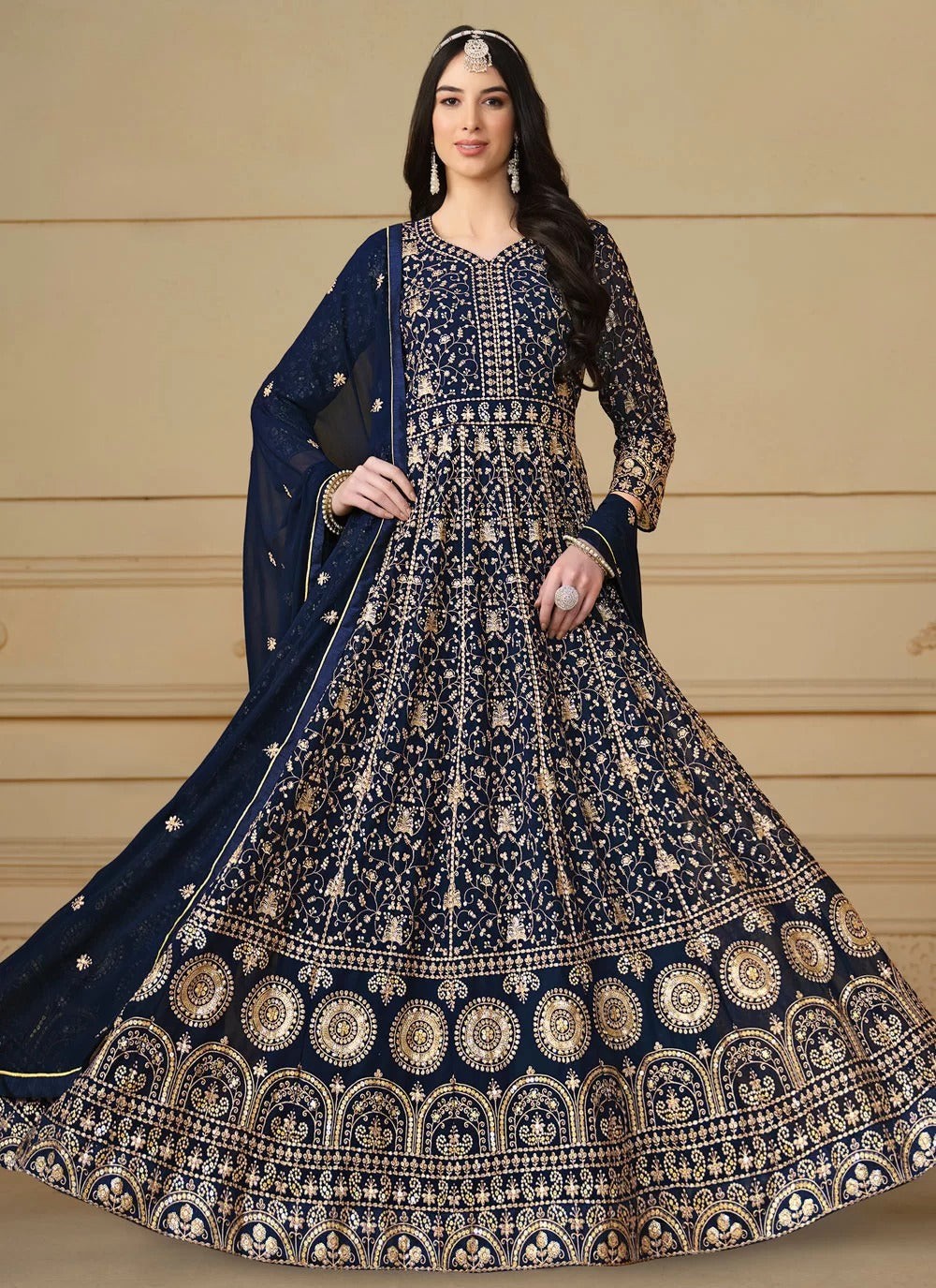 Woman wearing a navy blue and gold embroidered traditional outfit with a beige background