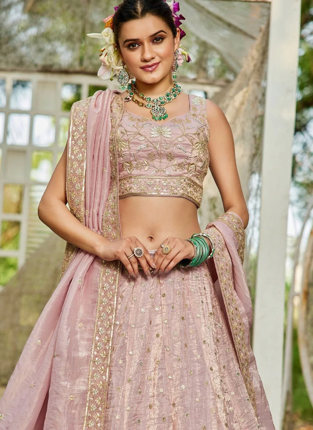 Woman in a traditional pink and gold outfit with jewelry outdoors.