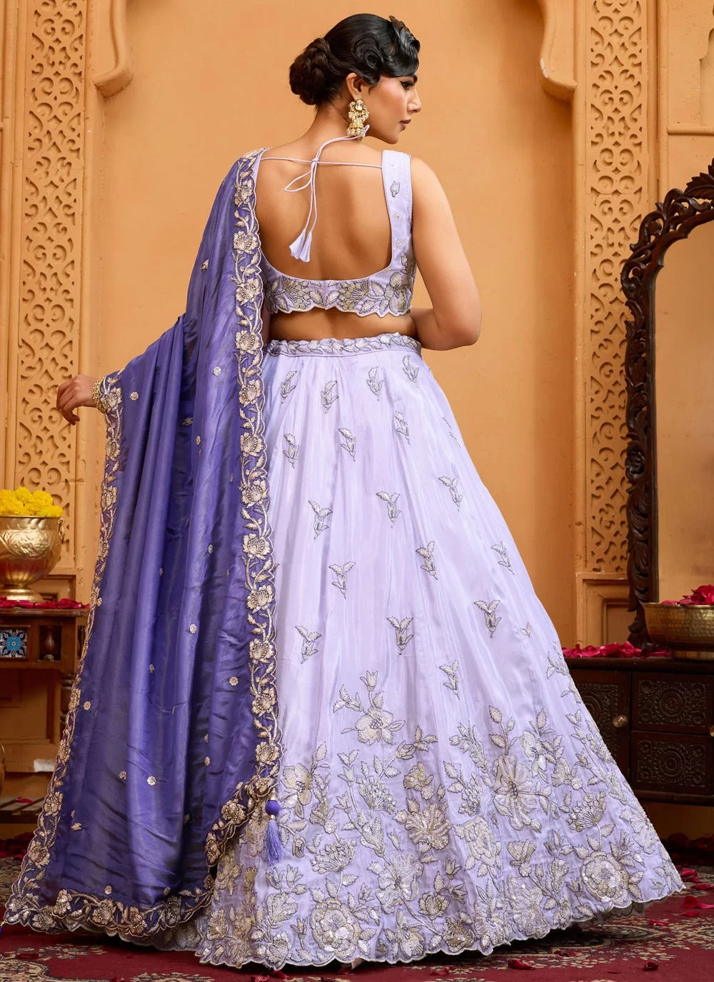 Woman in a white embroidered lehenga with a purple dupatta in an ornate setting