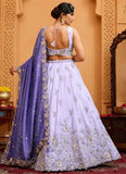 Woman in a white embroidered lehenga with a purple dupatta in an ornate setting
