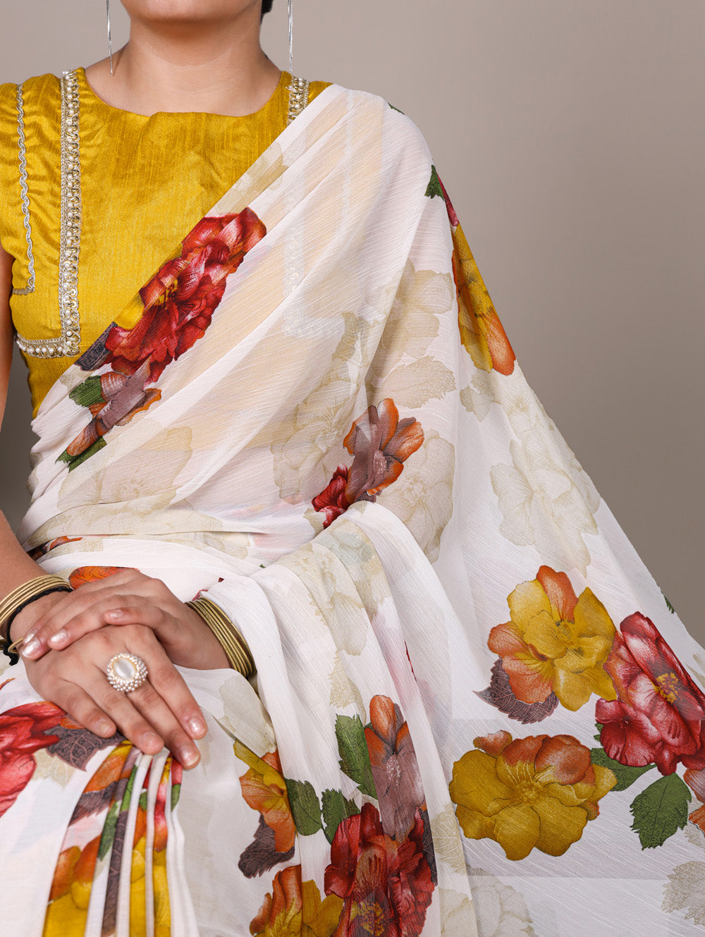 Woman wearing a white saree with floral patterns and a yellow blouse.
