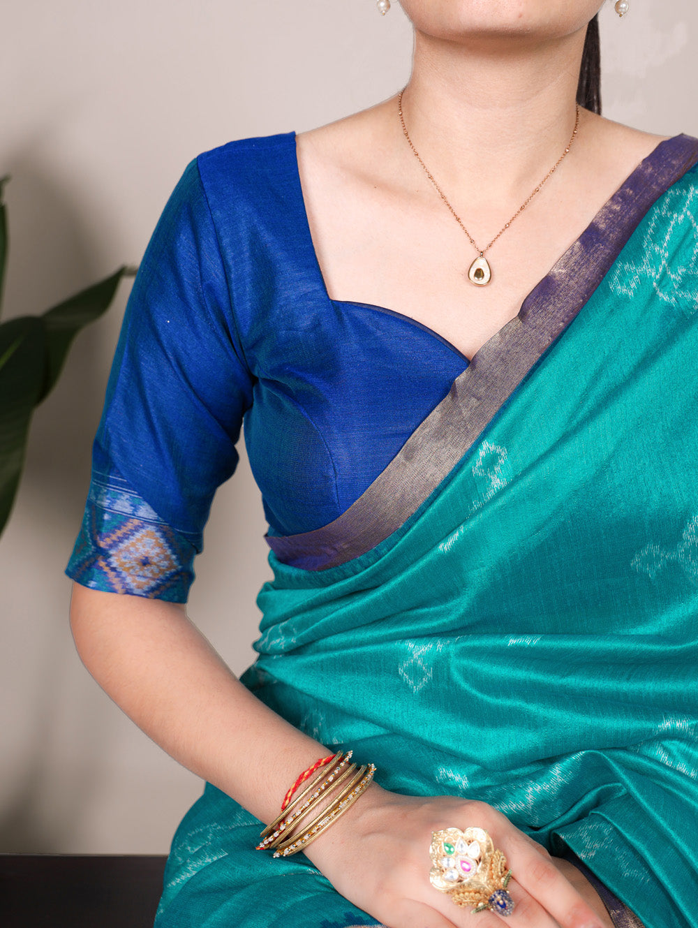 Person wearing a blue blouse and green saree with jewelry against a neutral background