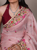 Woman wearing a pink saree with intricate embroidery and a maroon blouse.