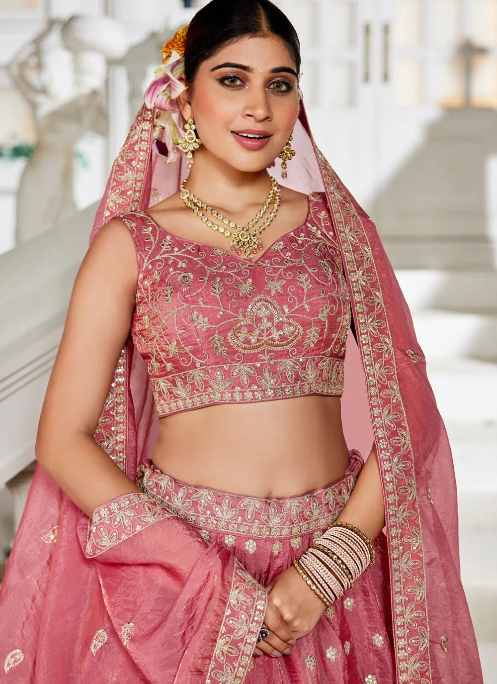 Woman in a traditional pink embroidered outfit with jewelry indoors