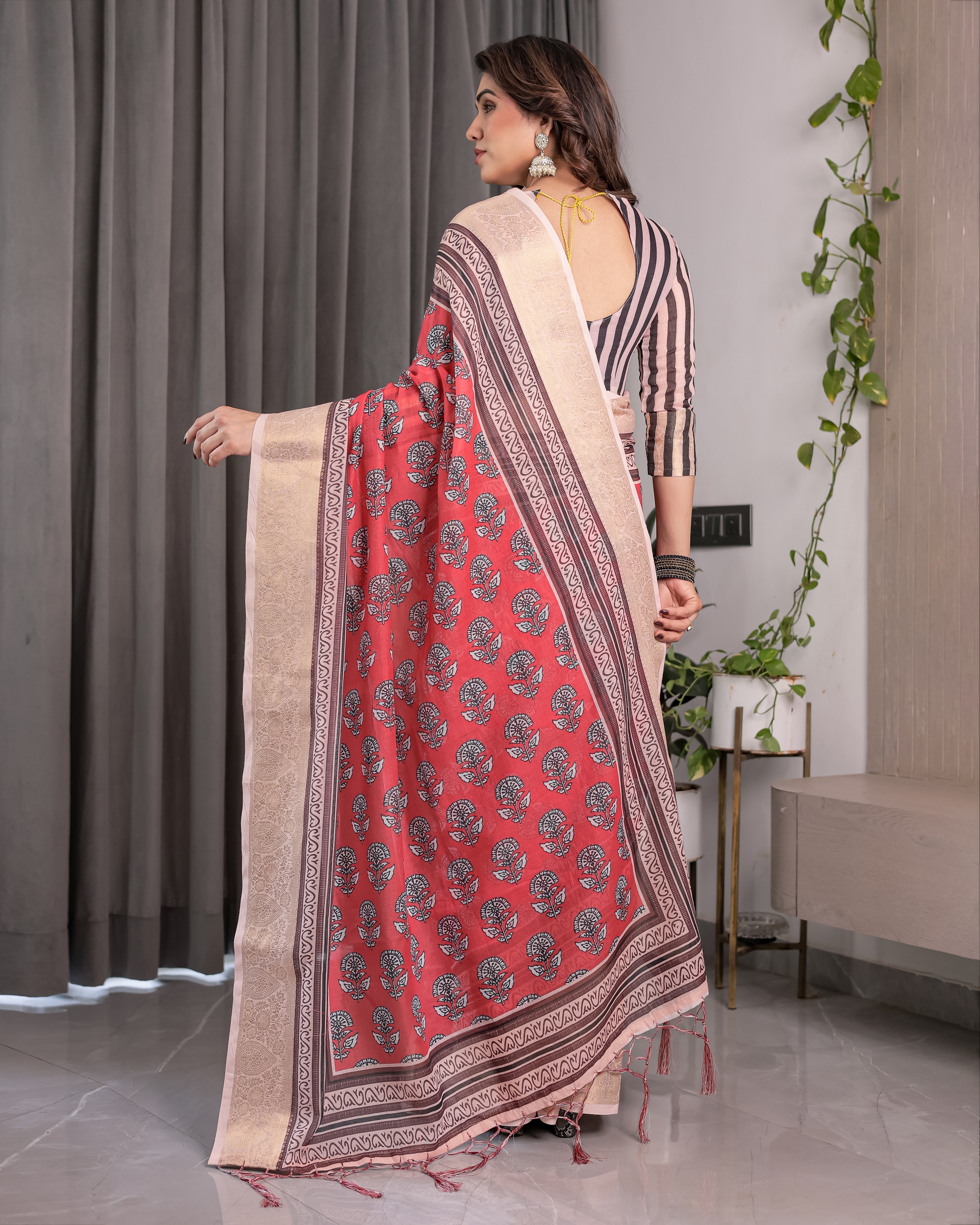 Woman wearing a red and beige saree with a pattern, standing indoors.