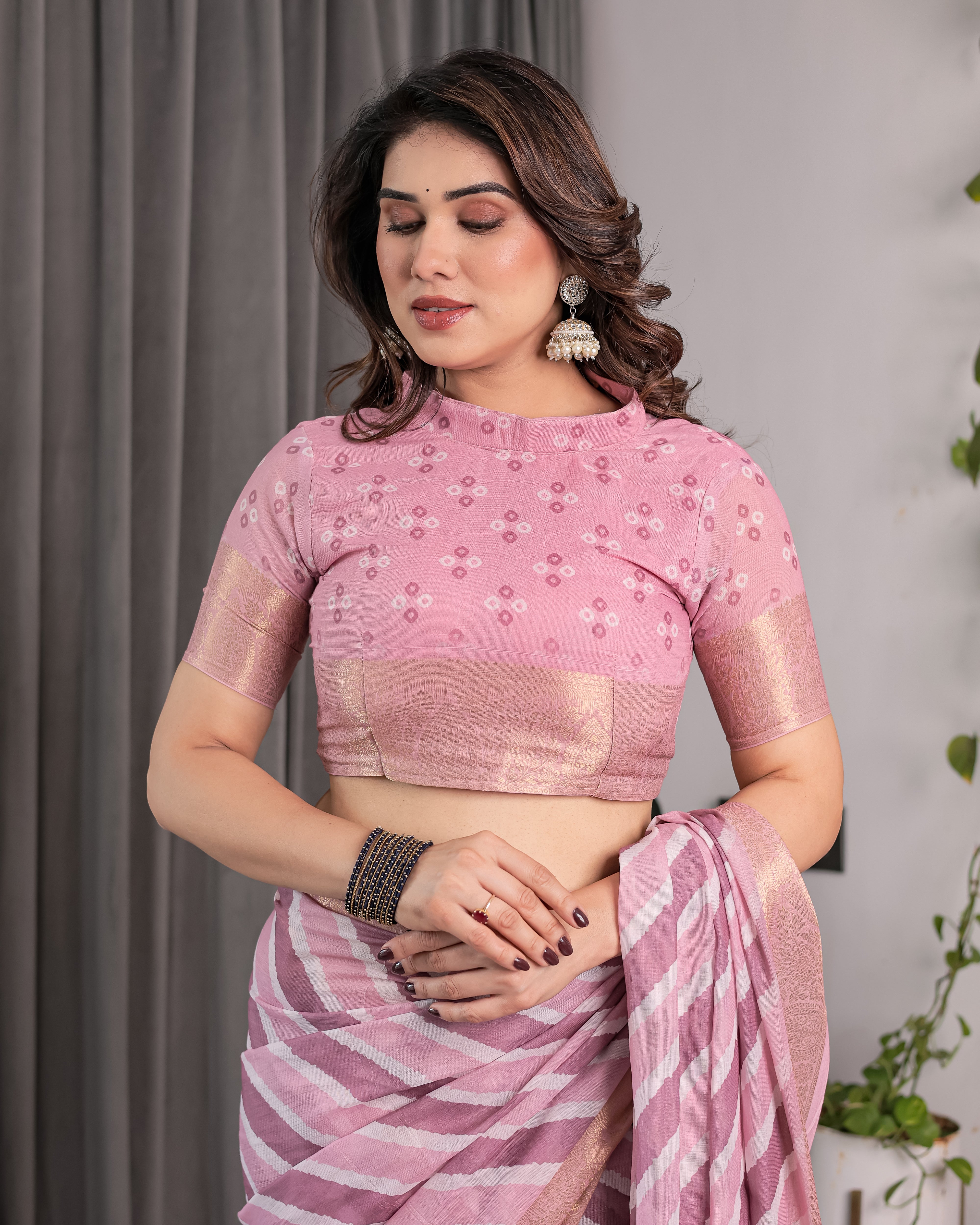 Woman wearing a pink saree with a matching blouse against a gray curtain background