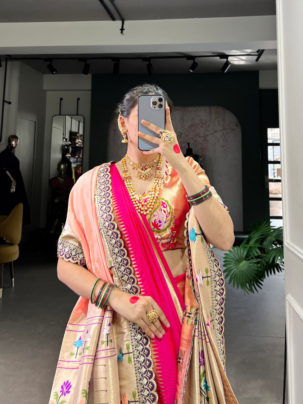 Woman taking a mirror selfie wearing a traditional saree with jewelry indoors.