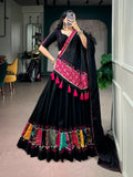 A woman takes a mirror selfie wearing a black traditional Indian lehenga choli with vibrant pink, red, and multicolor embroidered borders and tassels, set in an indoor boutique environment.