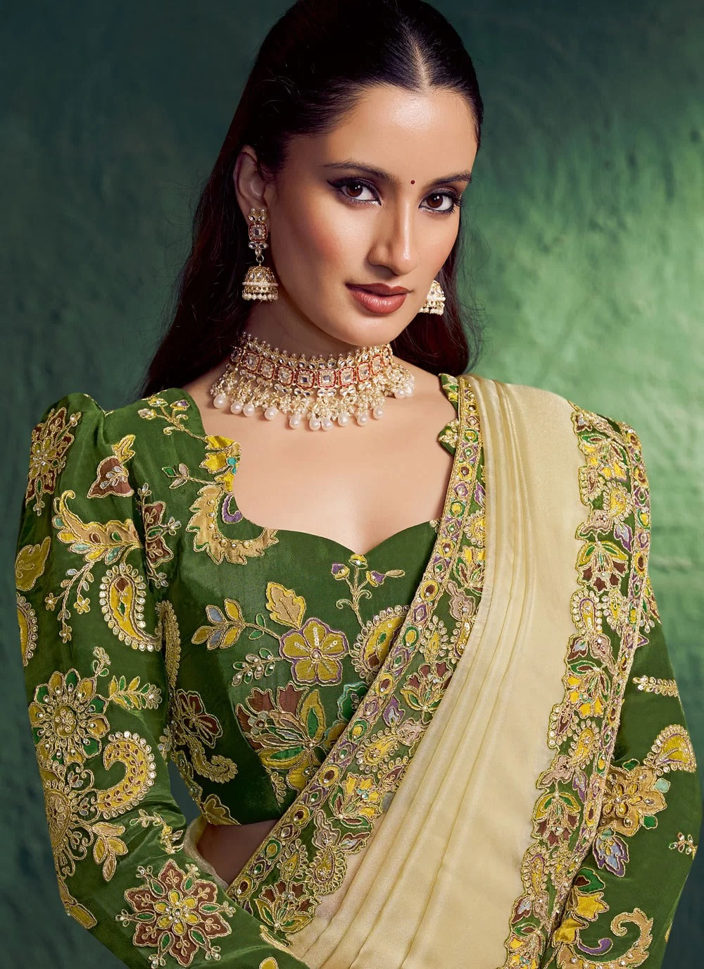 Woman wearing a green and gold embroidered saree with jewelry against a green background