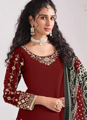 Woman wearing a maroon traditional outfit with gold embroidery and jewelry against a plain background