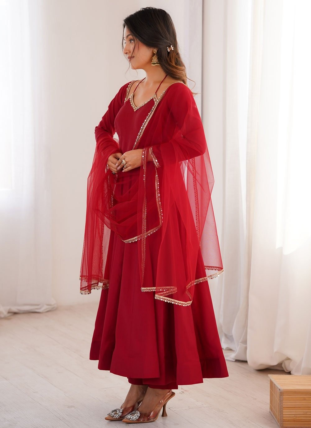 Woman wearing a red traditional outfit with gold details in a bright room.