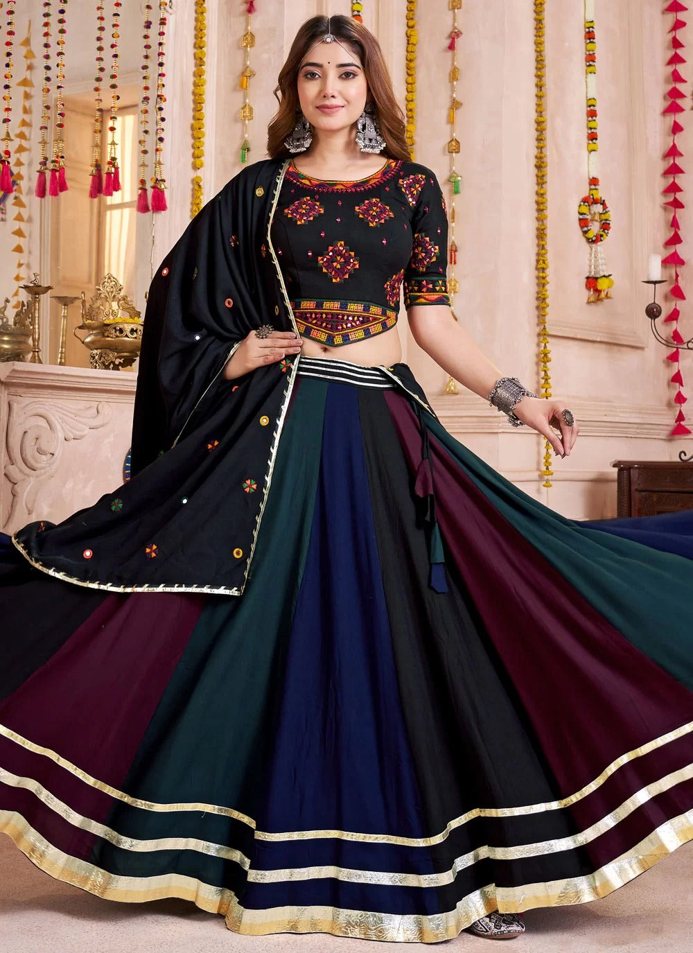 Woman wearing a traditional black and blue outfit with gold accents in a decorated room.