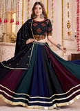 Woman wearing a traditional black and blue outfit with gold accents in a decorated room.